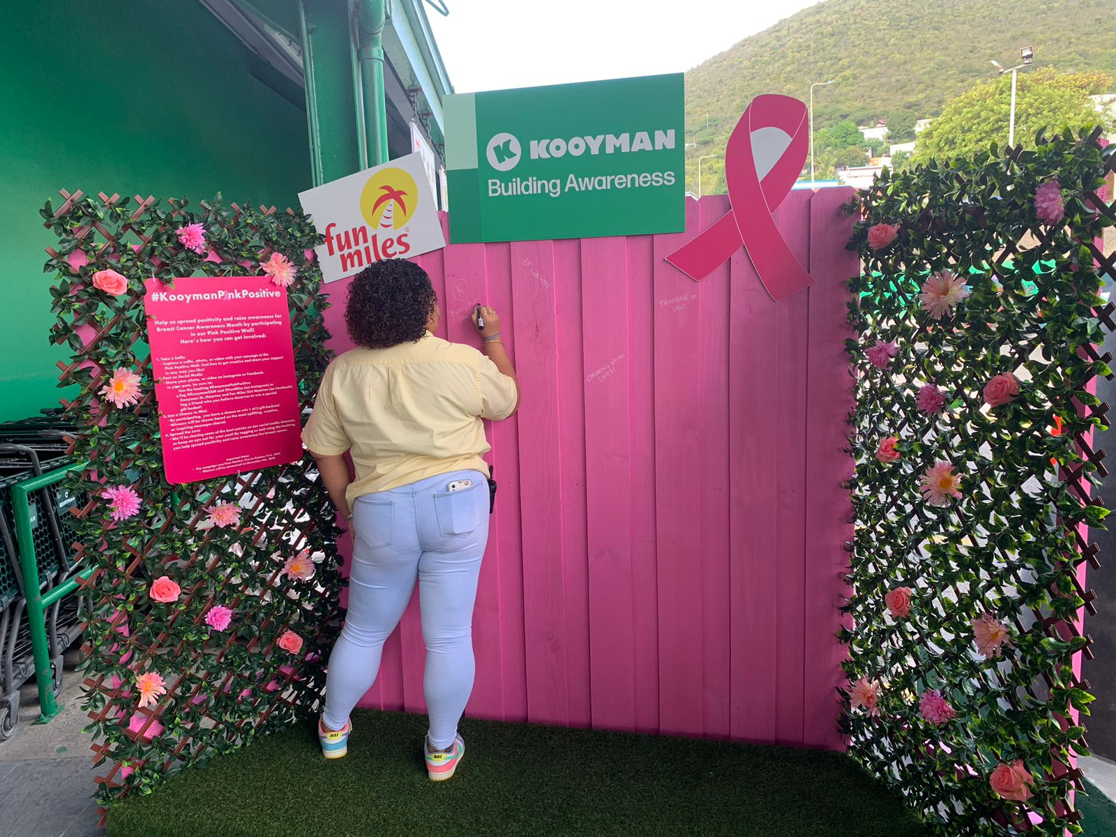 Alt Text: an employee volunteer contributing to the pink wall creating awareness around breast cancer.