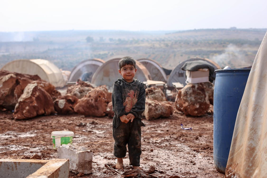 a little boy standing in the mud in a refugee camp