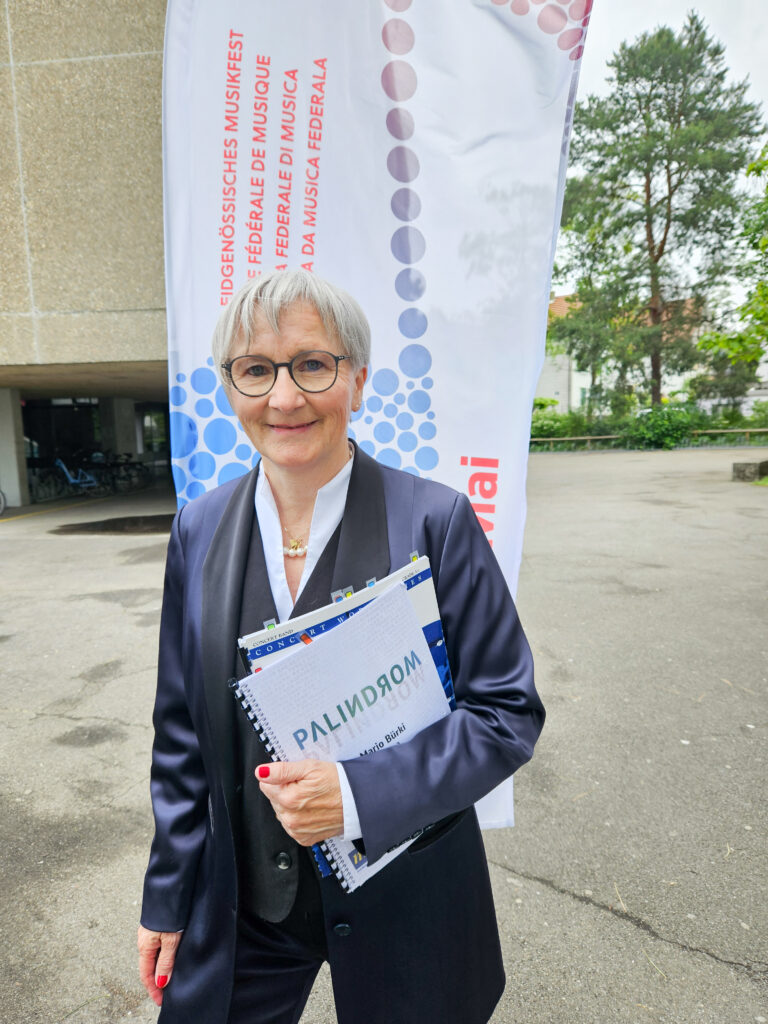 Emerita Blum-Duss mit Partituren unter dem Arm und EMF-Flagge im Hintergrund