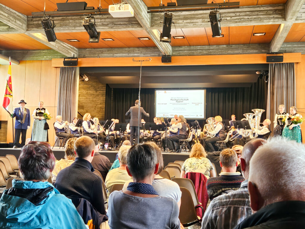 eine Musikgesellschaft auf der Bühne und viel Publikum im Saal