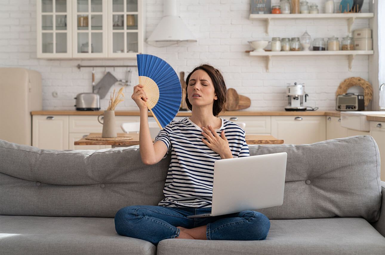 Woman using a fan in summer heat due to a broken air conditioner