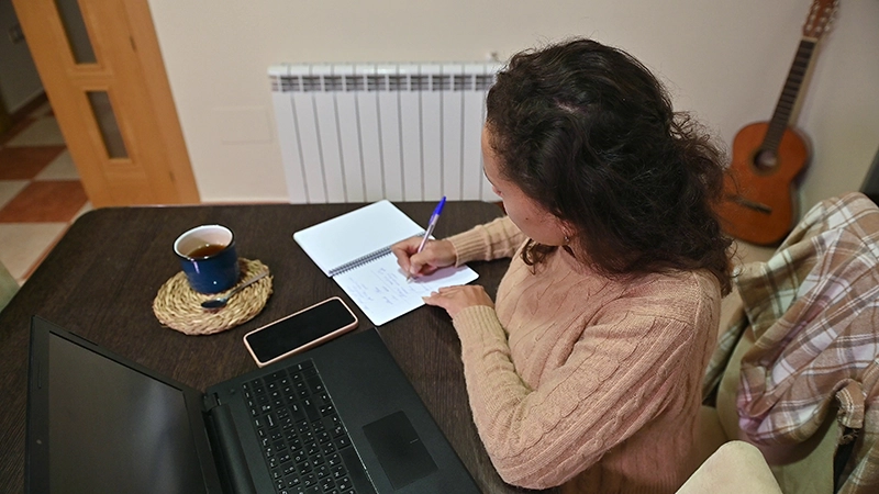 woman working from home taking notes with a cup of coffee and computer