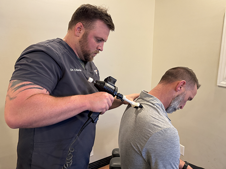 chiropractor dr. chavis adjusts a patient's back with theragun