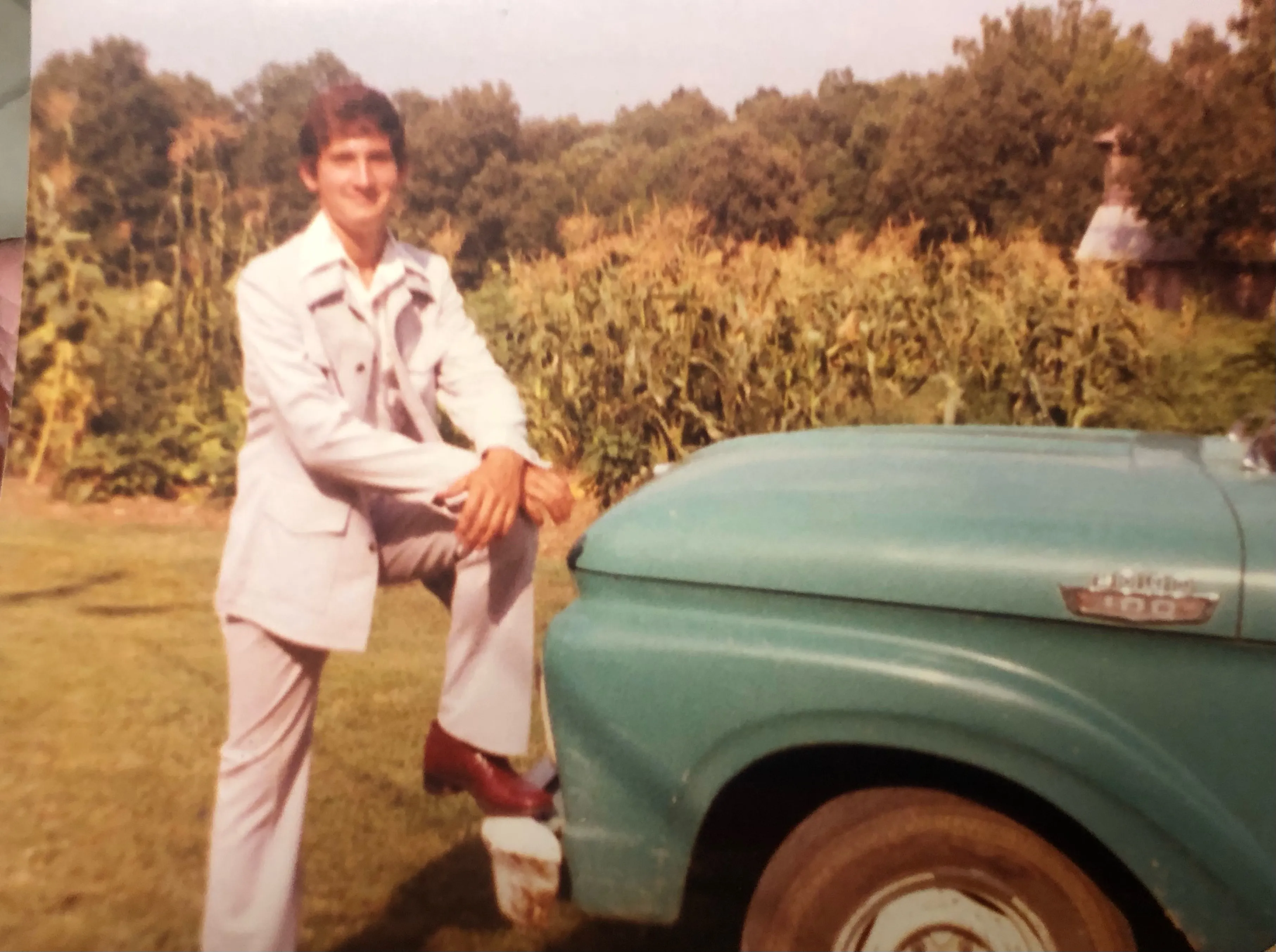 A man in a suit leaning on a truck.