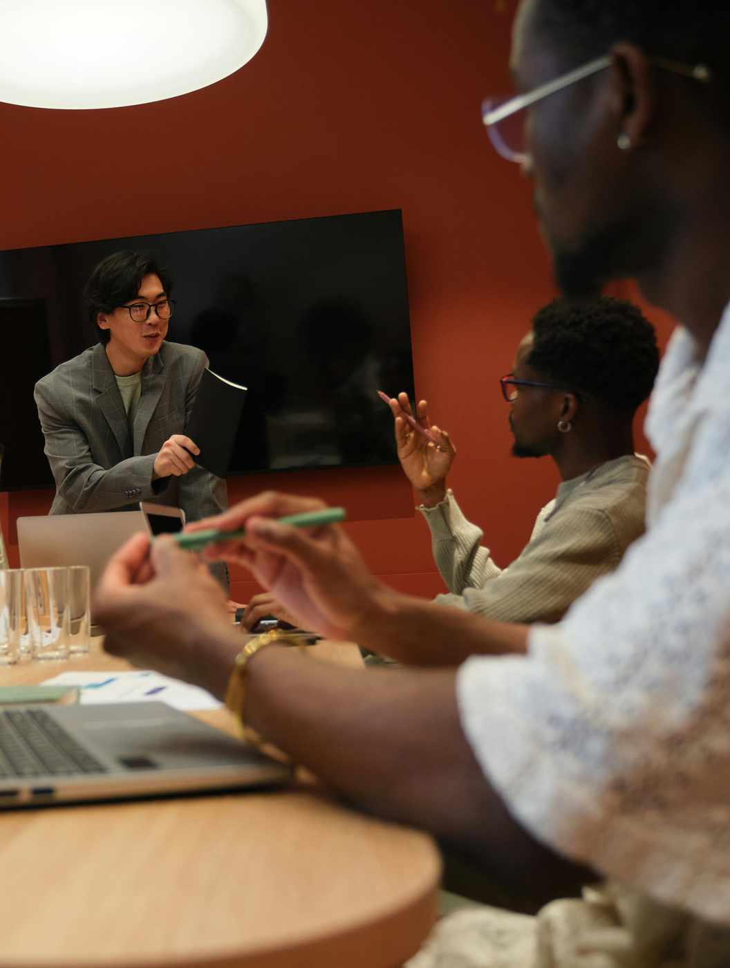 A diverse group of three team members, one at the head of the table and two seated on the sides, converse in a conference room—gesturing and sharing ideas.