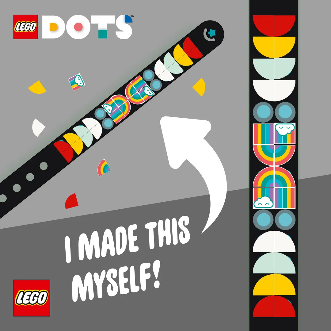A black LEGO DOTS wristband on a gray background, adorned with colorful tiles in patterns such as rainbows and smiling faces, with a white arrow graphic pointing upwards and text that reads, "I MADE THIS MYSELF!"