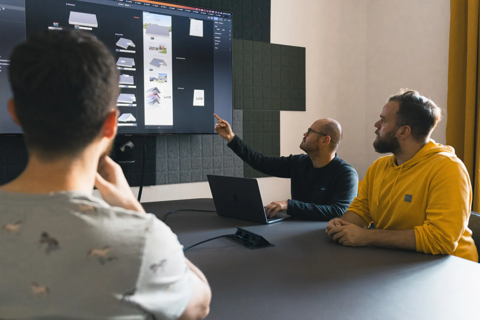 Two people working at desks with dual monitors in a modern office with wooden floors and white walls.