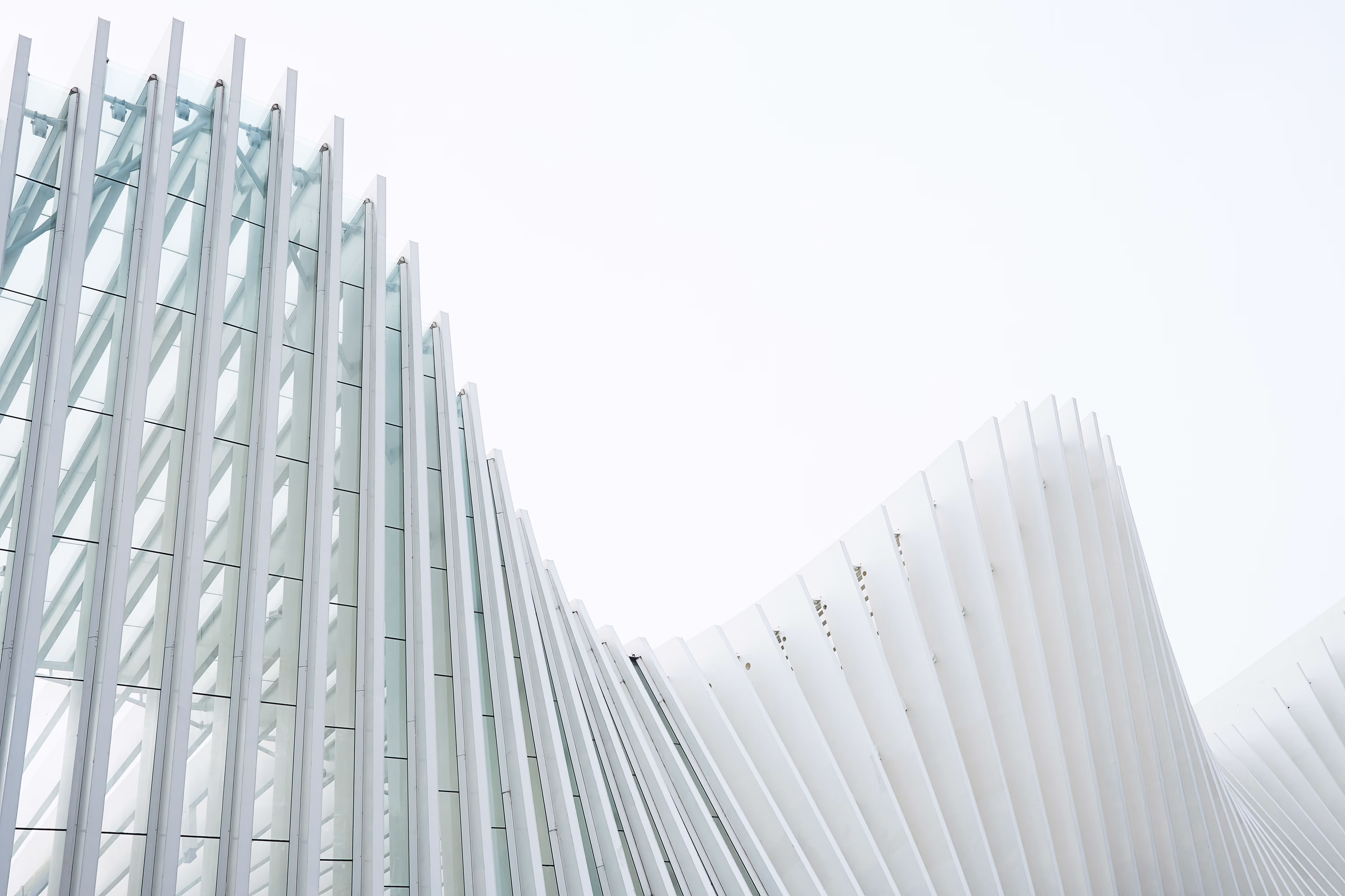 Curved modern architectural structure with vertical white and glass panels against a bright sky.