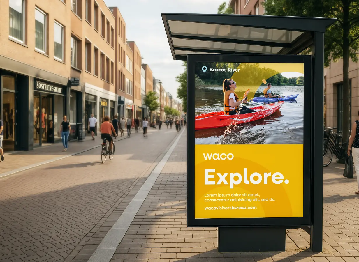 Outdoor city street with people walking and cycling, featuring a bus stop ad for Waco's Brazos River kayaking activity.