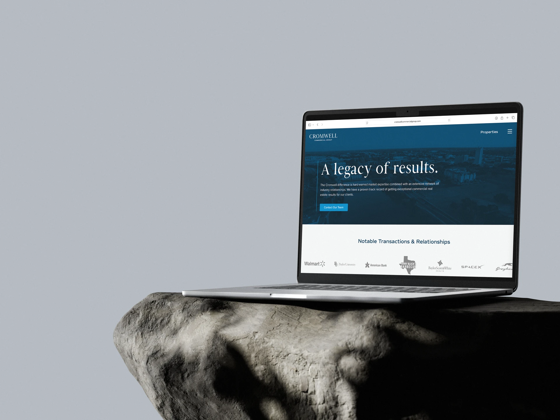 Open laptop displaying Cromwell Commercial Group website on a textured rock pedestal against a plain gray background.
