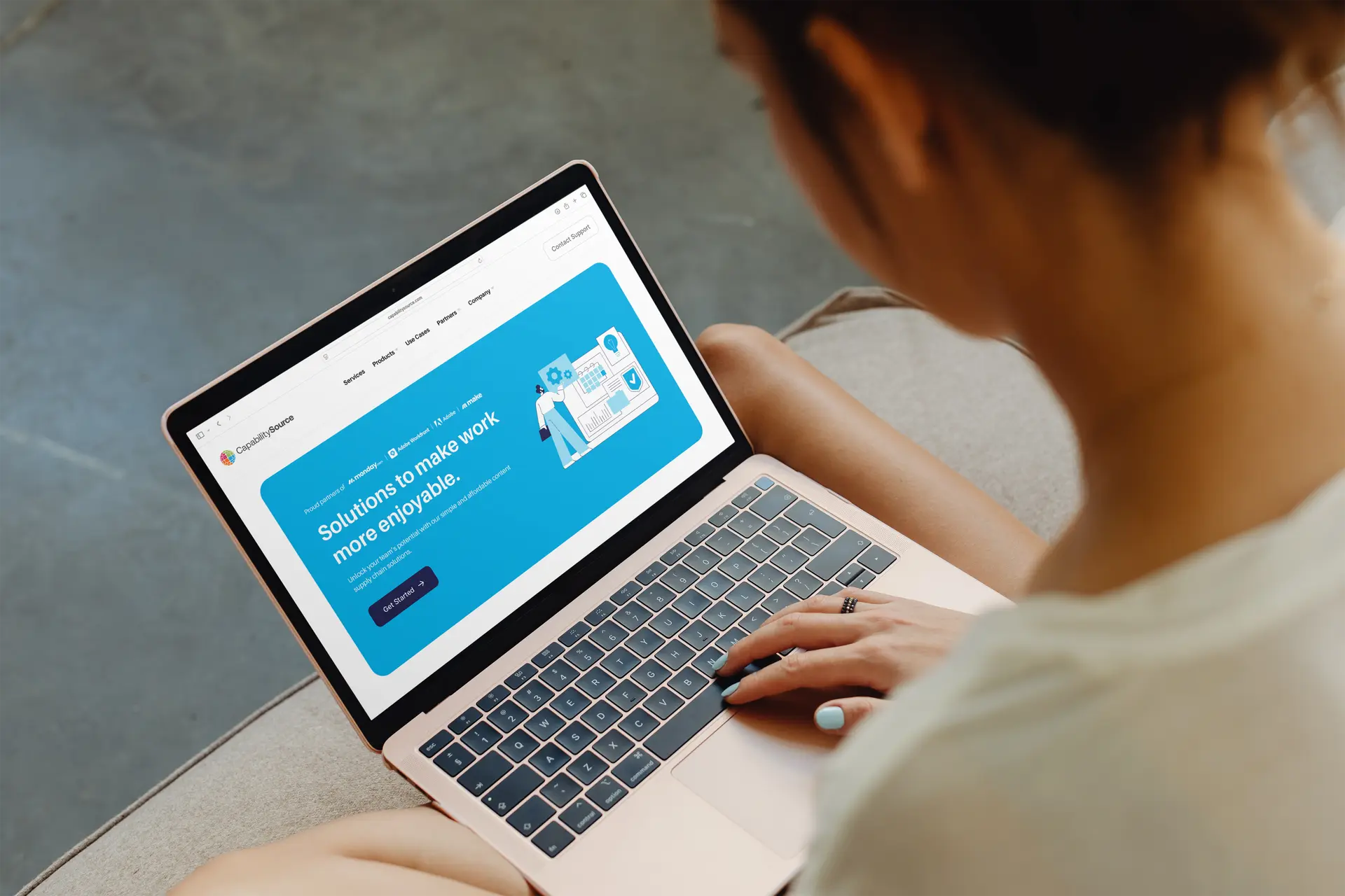 Person using a rose gold laptop showing a blue webpage with the text 'Solutions to make work more enjoyable.'