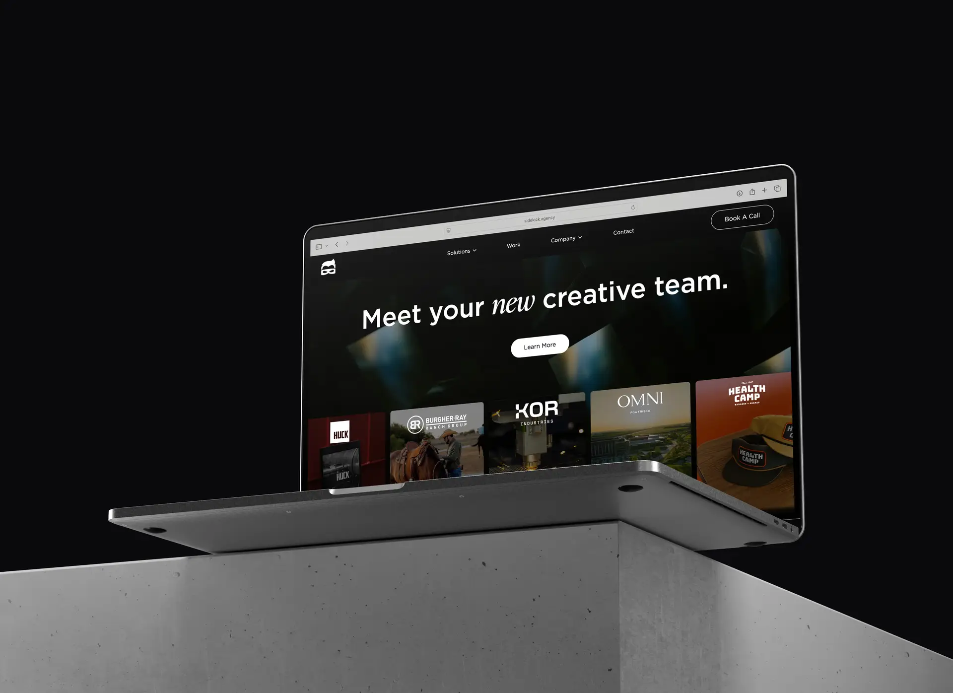 Laptop displaying a website homepage with the headline 'Meet your new creative team.' on a black background, placed on a gray concrete pedestal.