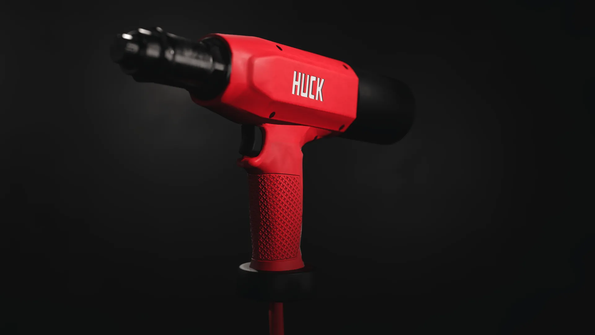 Red and black pneumatic tool with textured grip and the brand name Huck on the side, against a dark background.