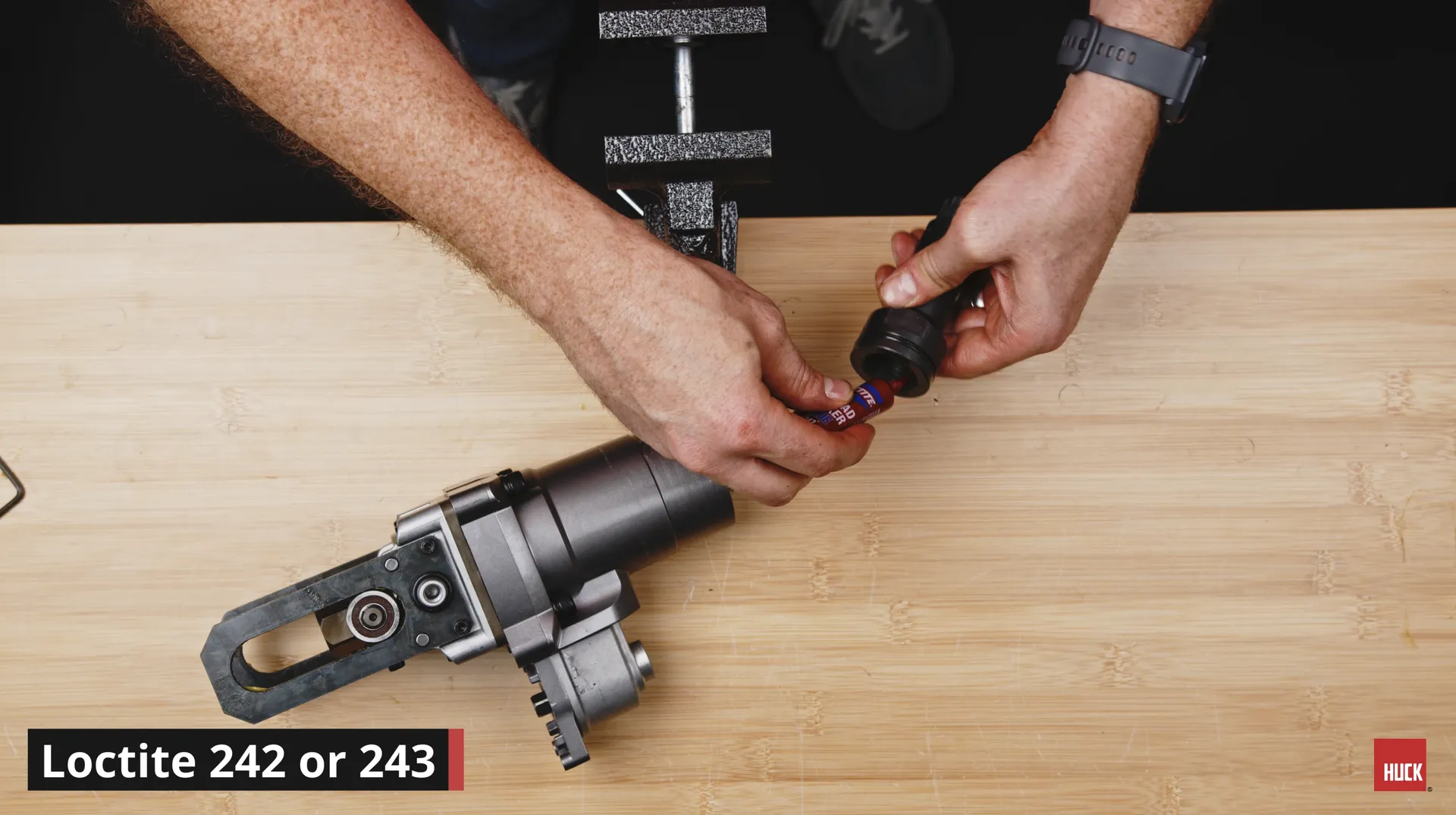 Hands holding a small bottle of Loctite threadlocker near a metal tool on a wooden surface.