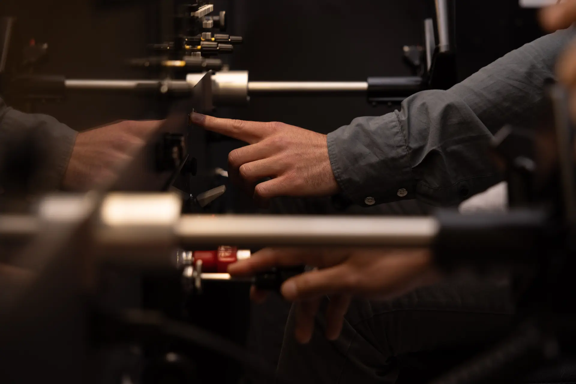 Person adjusting controls on a dark, complex optical or scientific instrument.