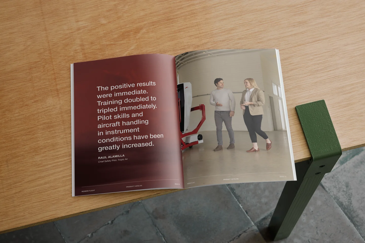 Open catalog on wooden table showing a testimonial and two people walking indoors next to equipment.