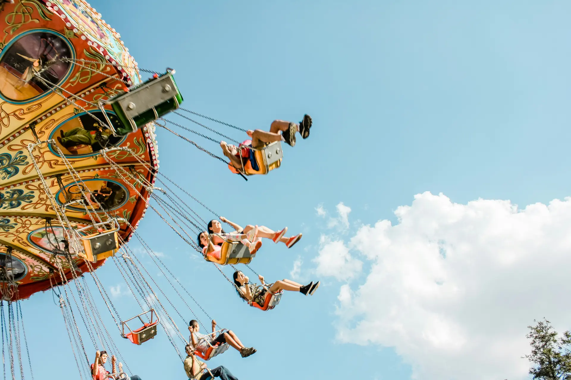 People enjoying swings on a colorful amusement park ride against a bright blue sky with clouds.