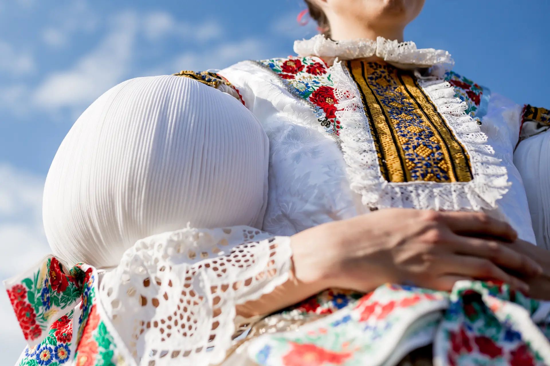 Person wearing detailed traditional embroidered clothing holding a large white pleated ball.