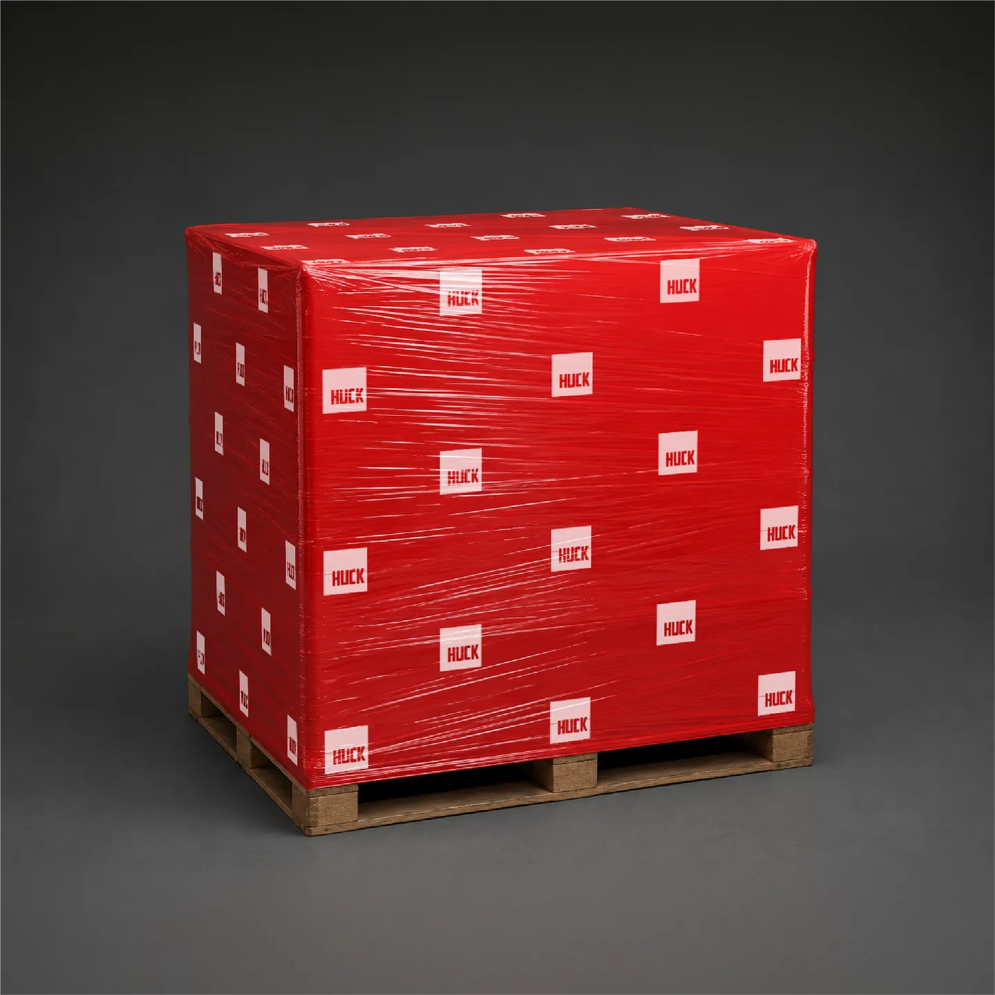 Red pallet-wrapped package marked with repeated white HUCK logos on a wooden pallet against gray background.