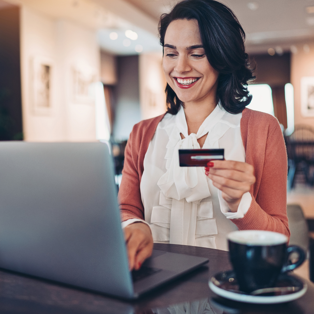 woman at laptop smiles while holding credit card shopping online