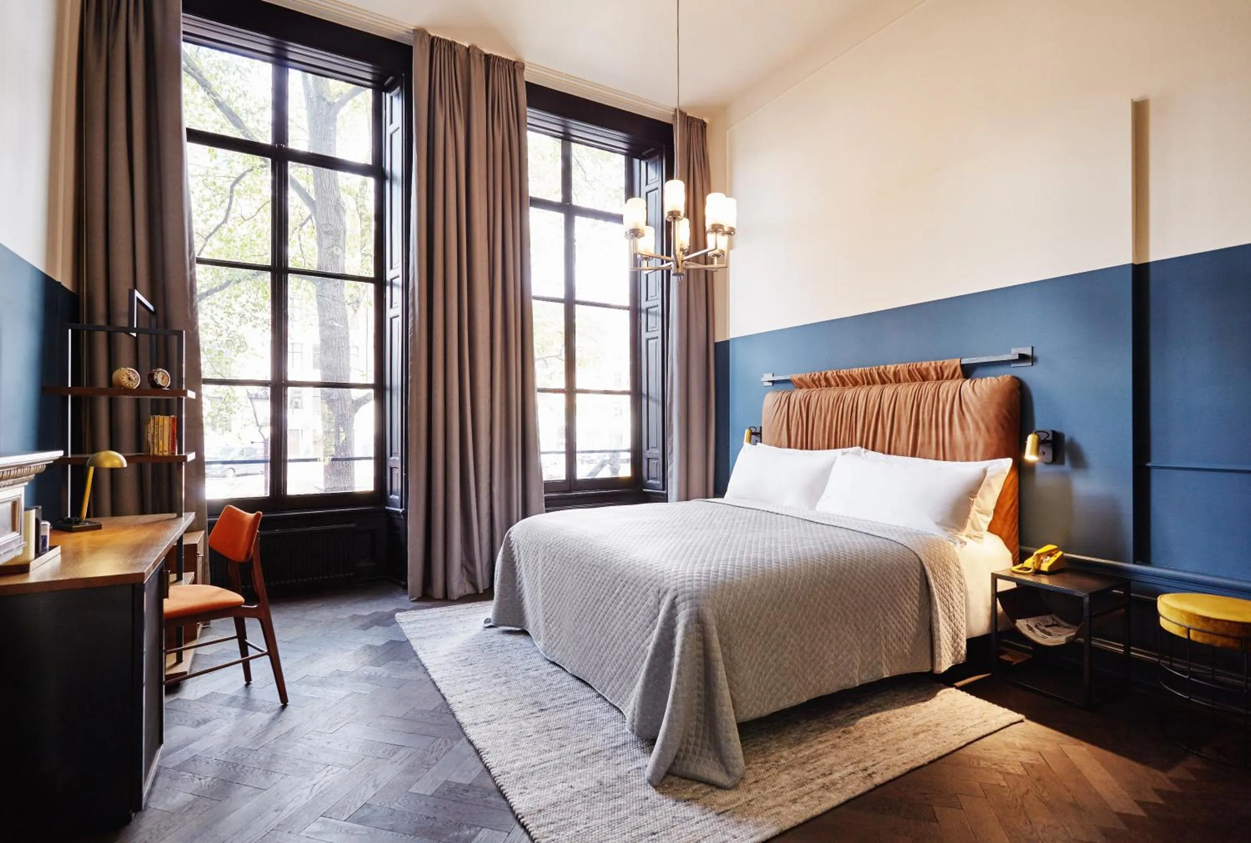 Guest room with two-tone blue walls, rust velvet headboard, parquet floor and vintage chandelier