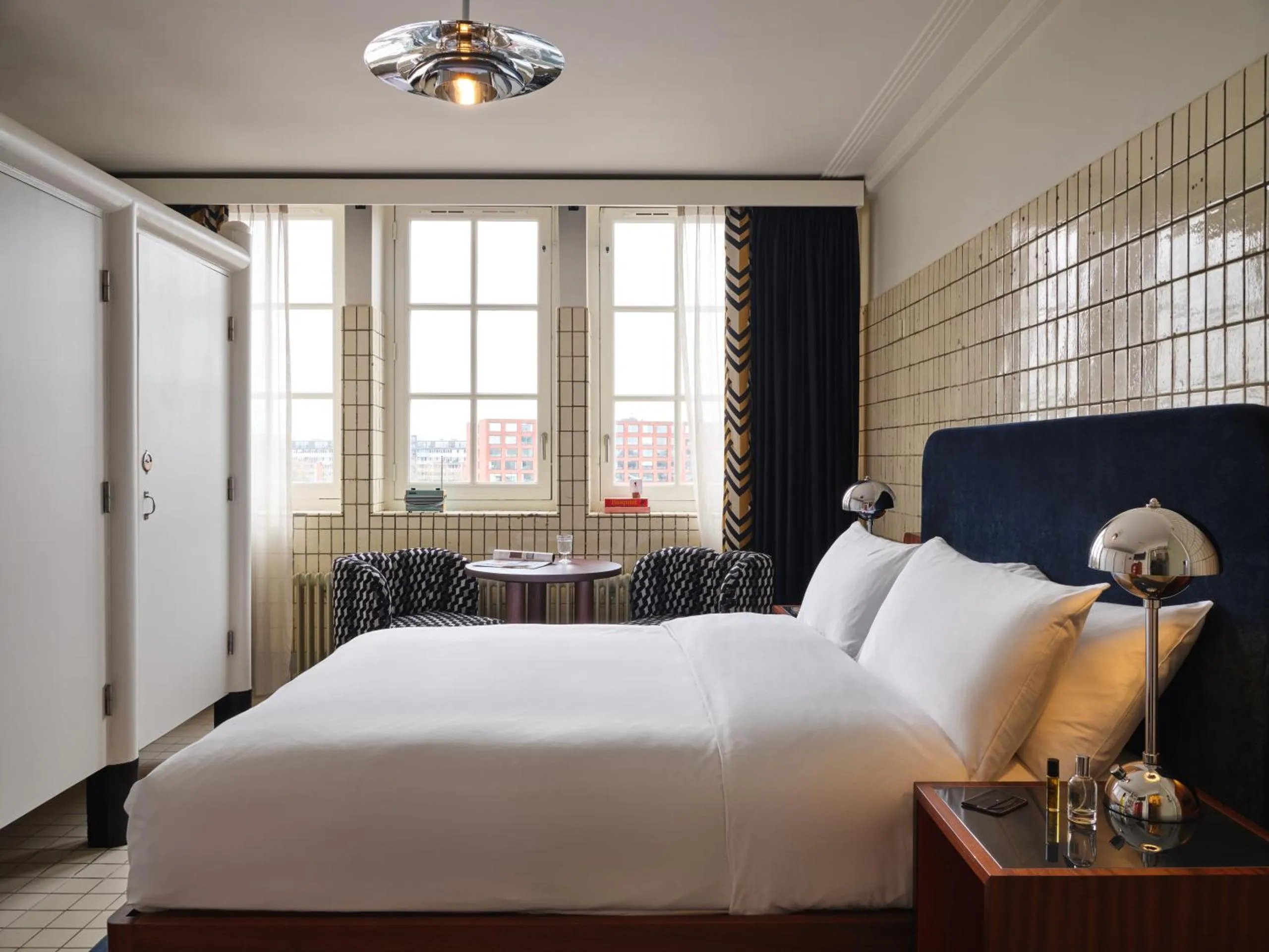 The Hoxton Lloyd Amsterdam bedroom with glazed brick tiled walls, navy velvet headboard and chrome ball lamps