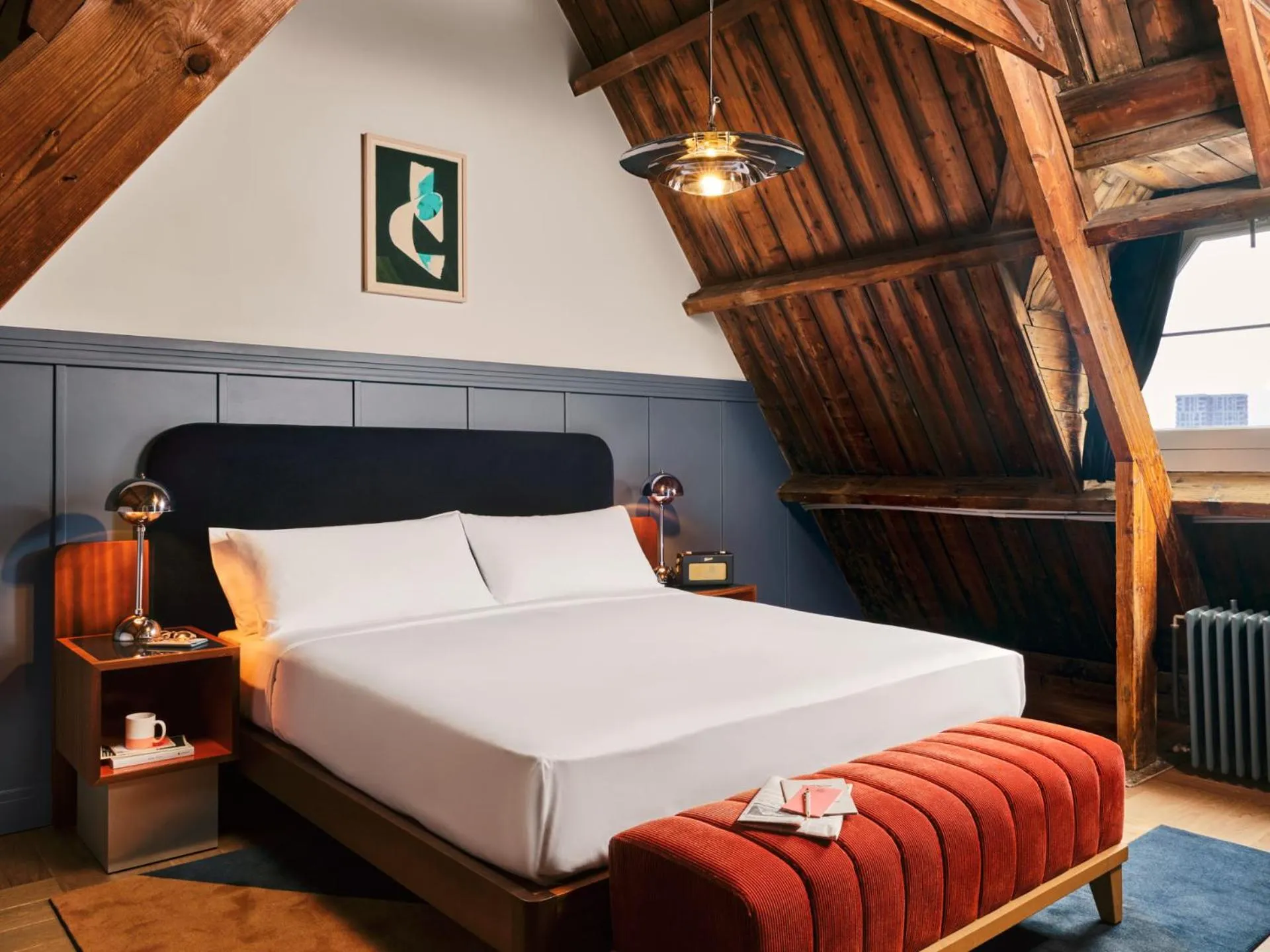 The Hoxton Lloyd Amsterdam loft bedroom with exposed timber beams, navy panelling and rust velvet bench