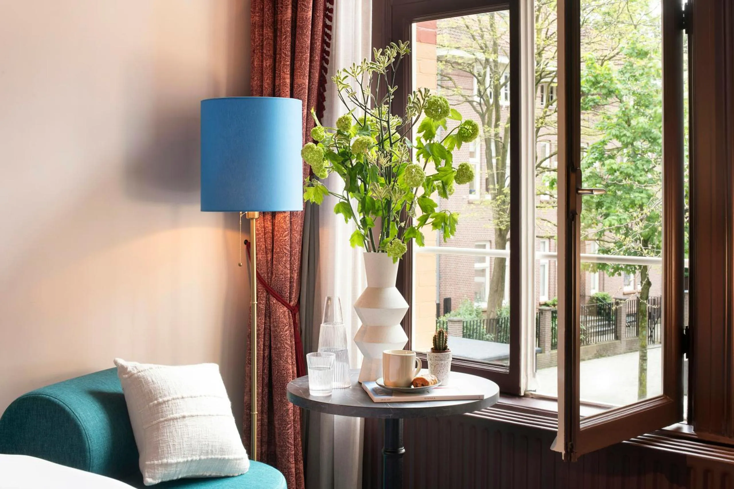 Jan Luyken Amsterdam guest room with teal armchair, blue lampshade and sculptural vase by an open window