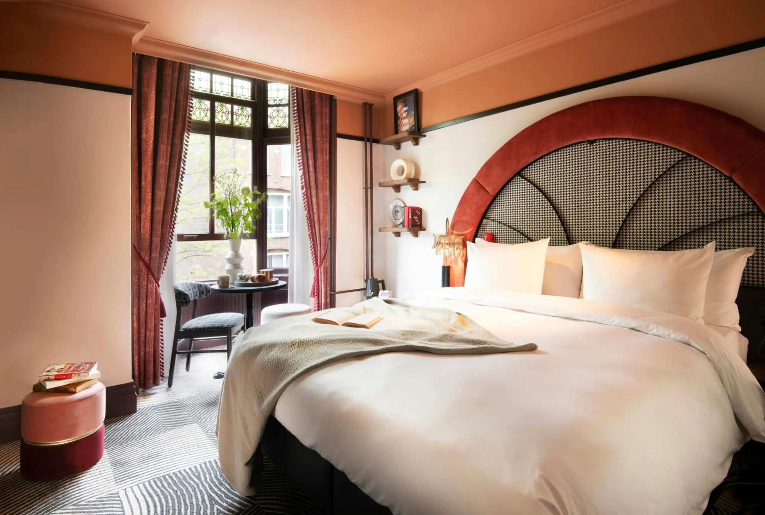 Jan Luyken Amsterdam bedroom with arched red velvet headboard, peach walls and stained glass window