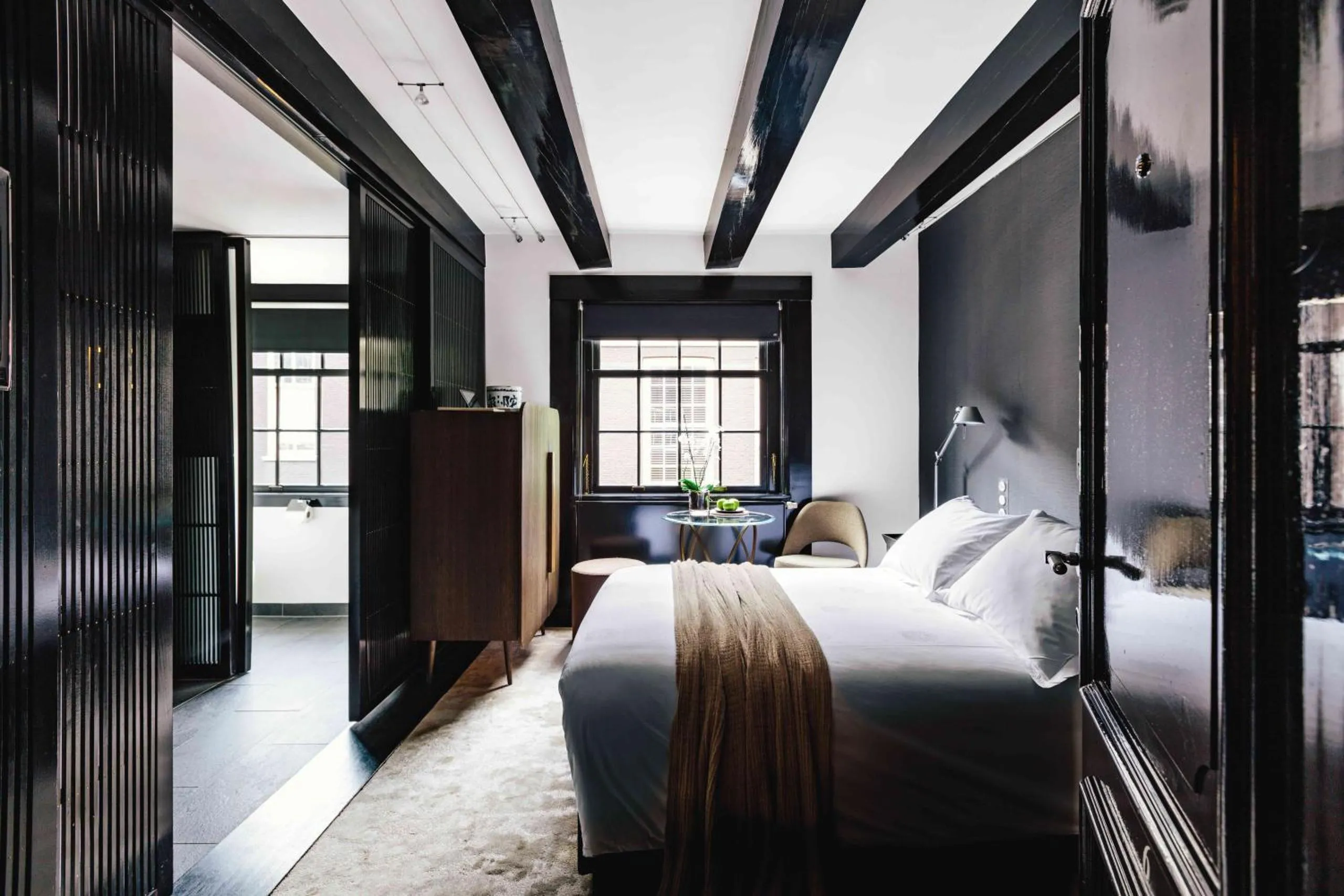The Dylan Amsterdam bedroom with high-gloss black lacquered beams, dark panelling and white linen