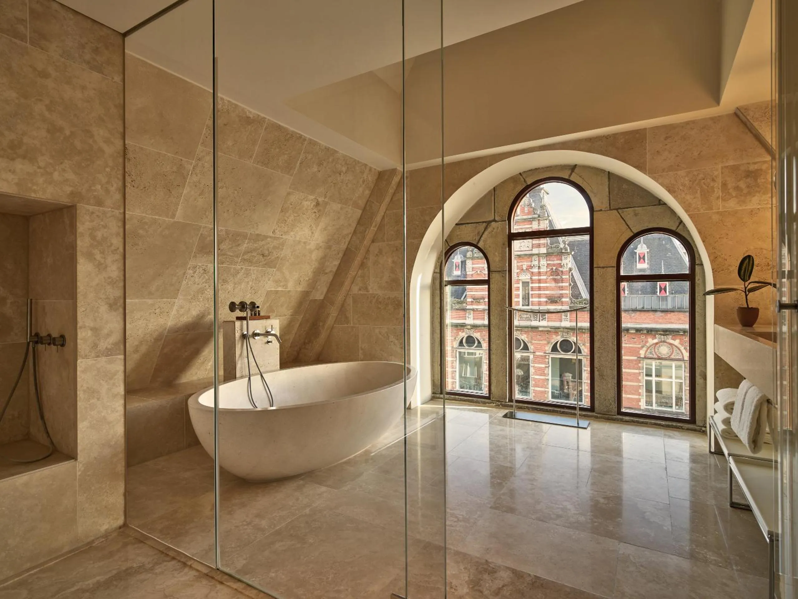 Conservatorium Amsterdam bathroom with travertine walls, freestanding stone tub and arched windows