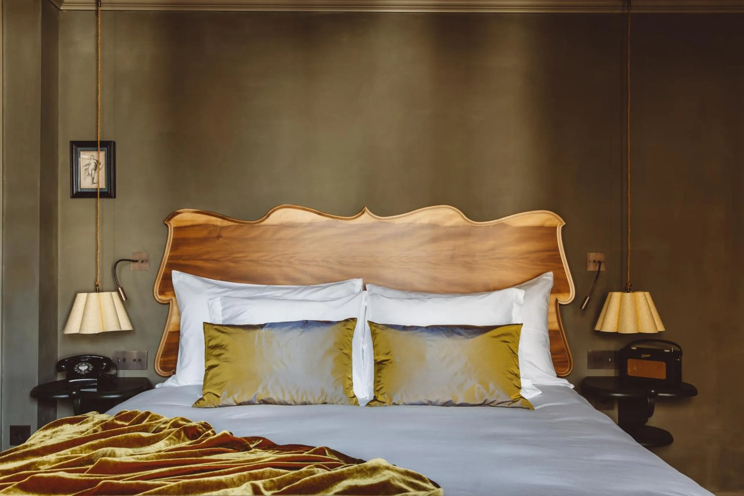 De Durgerdam bedroom with carved walnut headboard, olive walls and gold velvet pillows