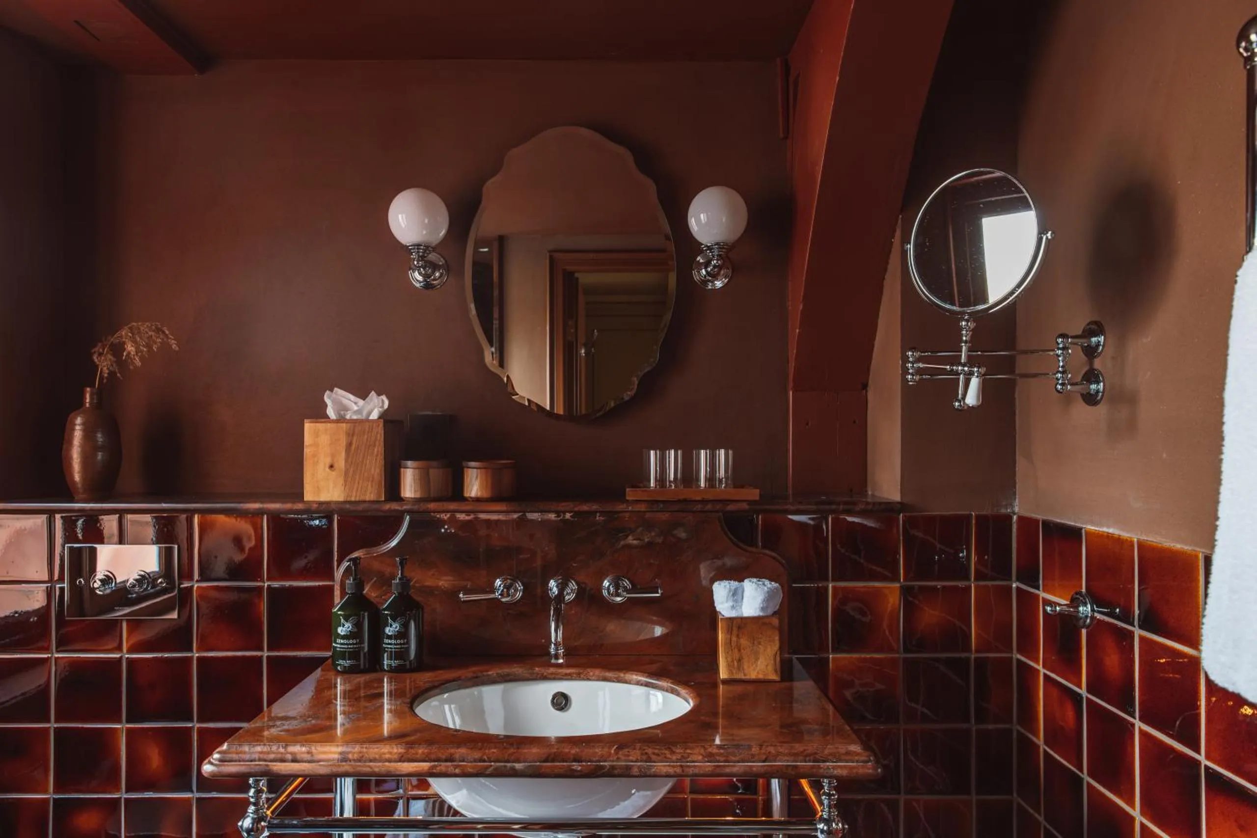 De Durgerdam bathroom with rust glazed tiles, marble vanity and a scalloped oval mirror