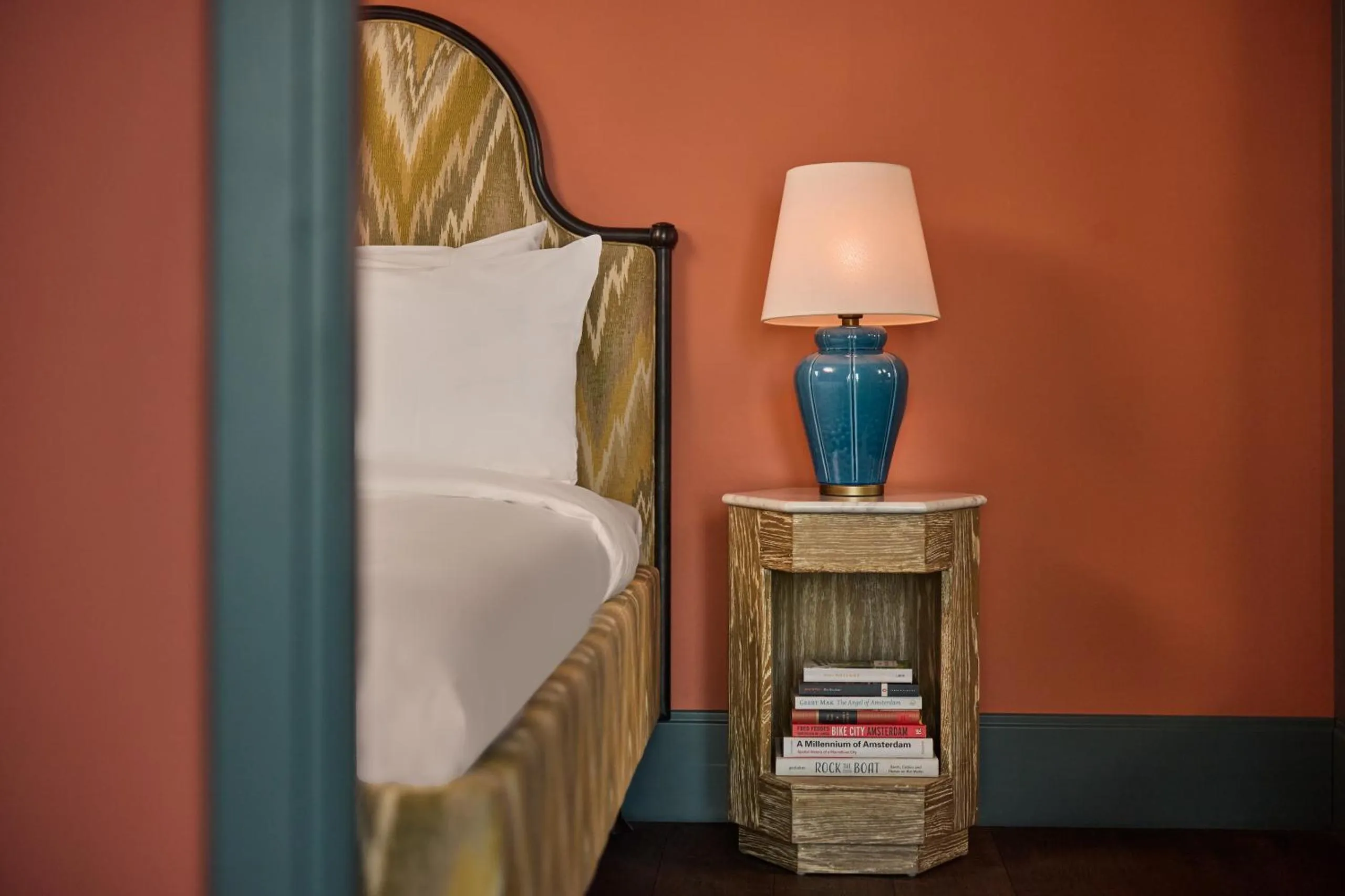 The July Boat & Co bedroom with chevron headboard, terracotta walls and a blue ceramic table lamp