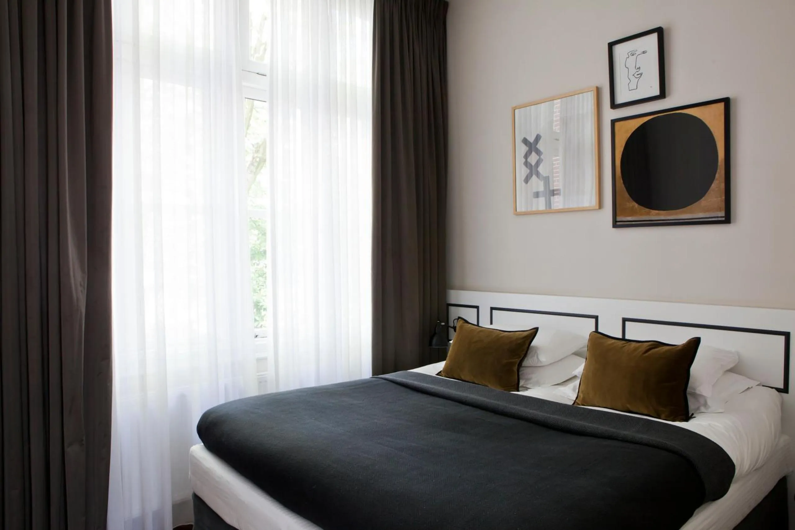 Morgan & Mees Amsterdam bedroom with monochrome gallery wall, ochre velvet pillows and sheer curtains
