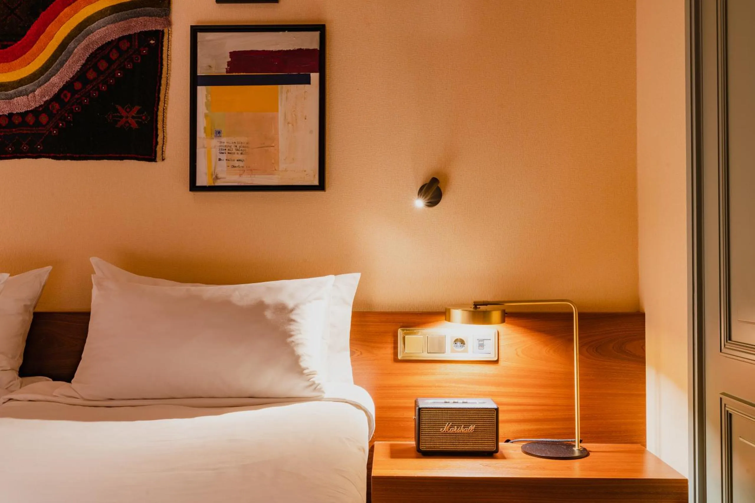 Hotel Mercier bedroom with peach walls, walnut headboard, vintage radio and brass desk lamp