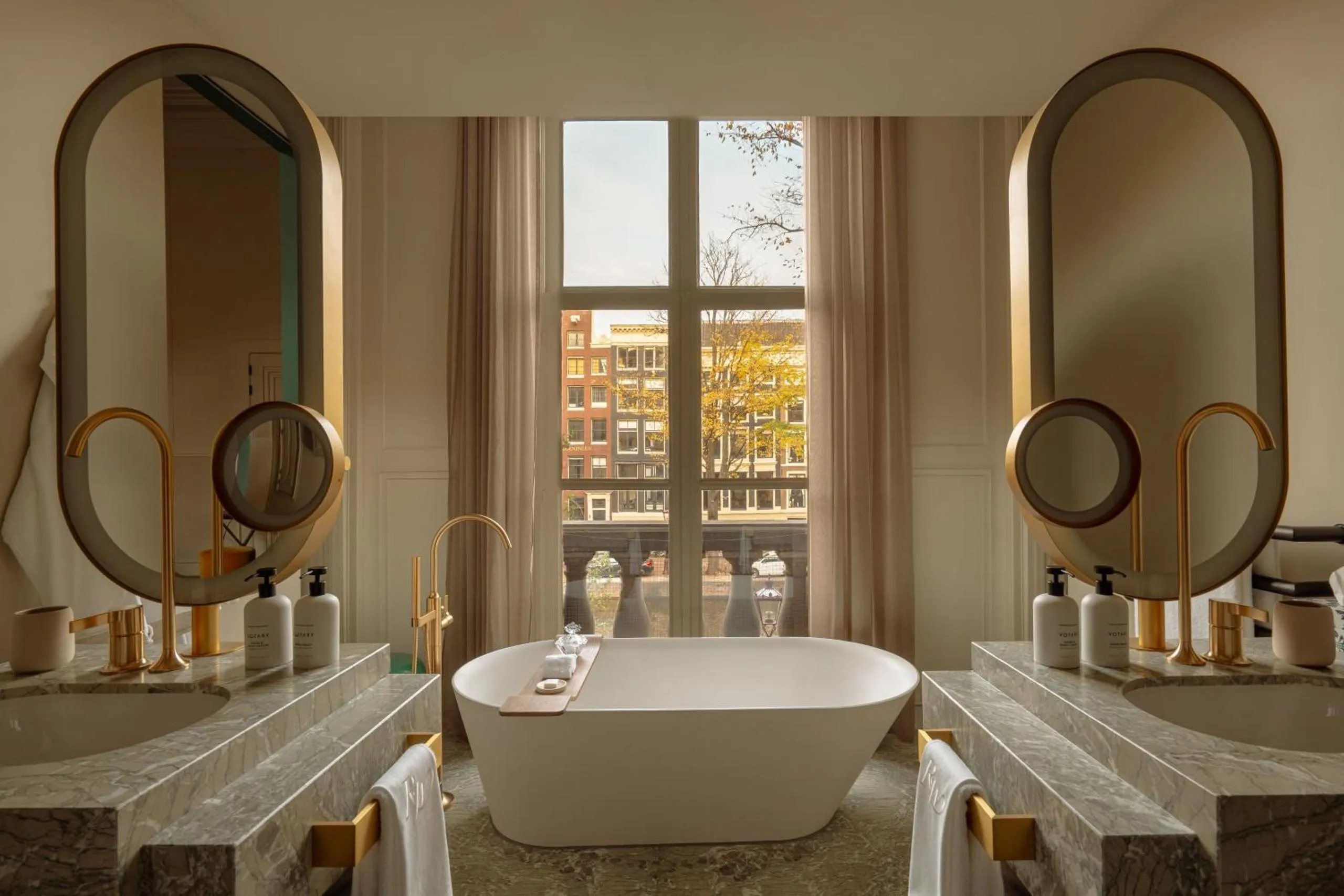 Rosewood Amsterdam bathroom with marble vanities, freestanding tub, brass fixtures and canal view