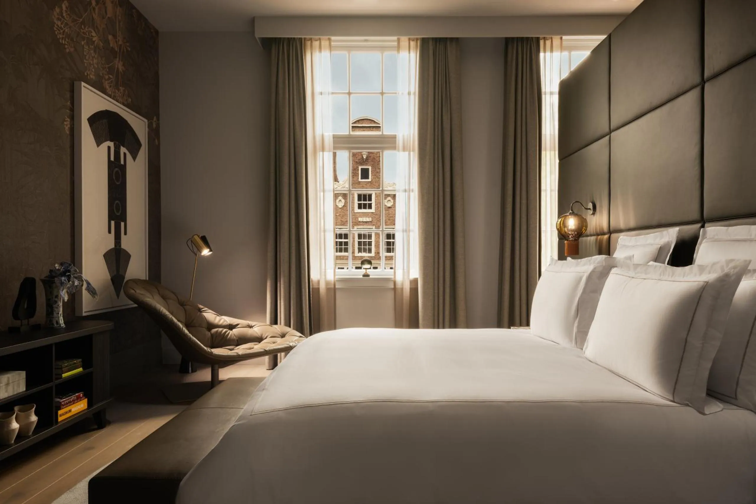 Rosewood Amsterdam bedroom with padded headboard wall, leather chaise and canal-house view