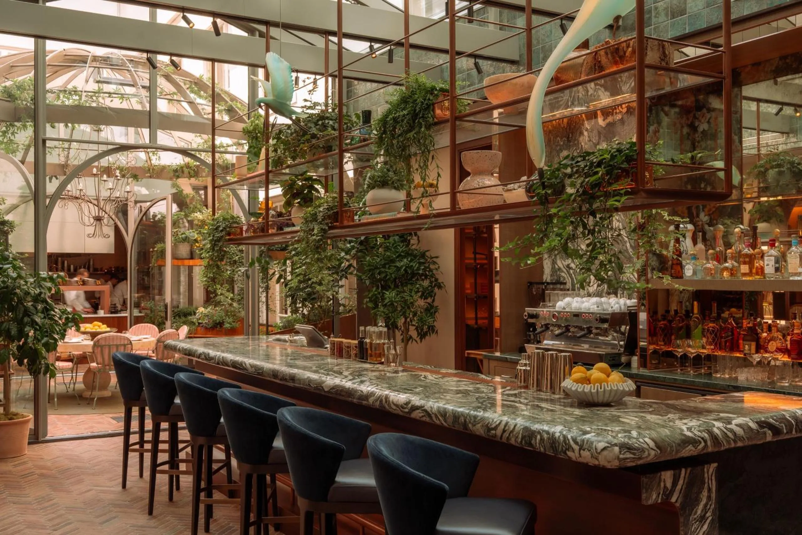Rosewood Amsterdam conservatory bar with green marble counter, glass roof and hanging greenery