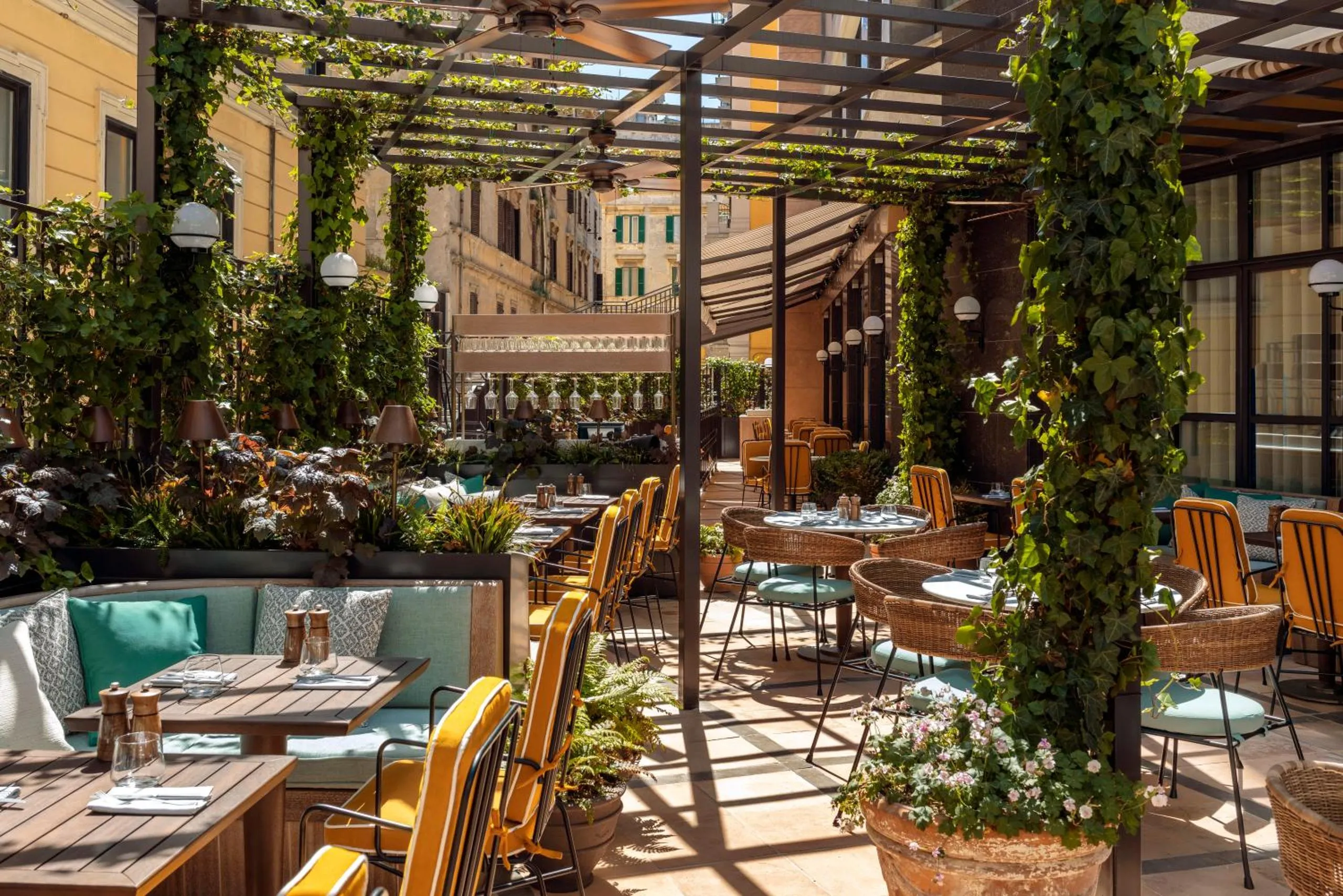 The Hoxton Rome outdoor terrace with ivy-covered pergola, yellow striped chairs and wicker seating