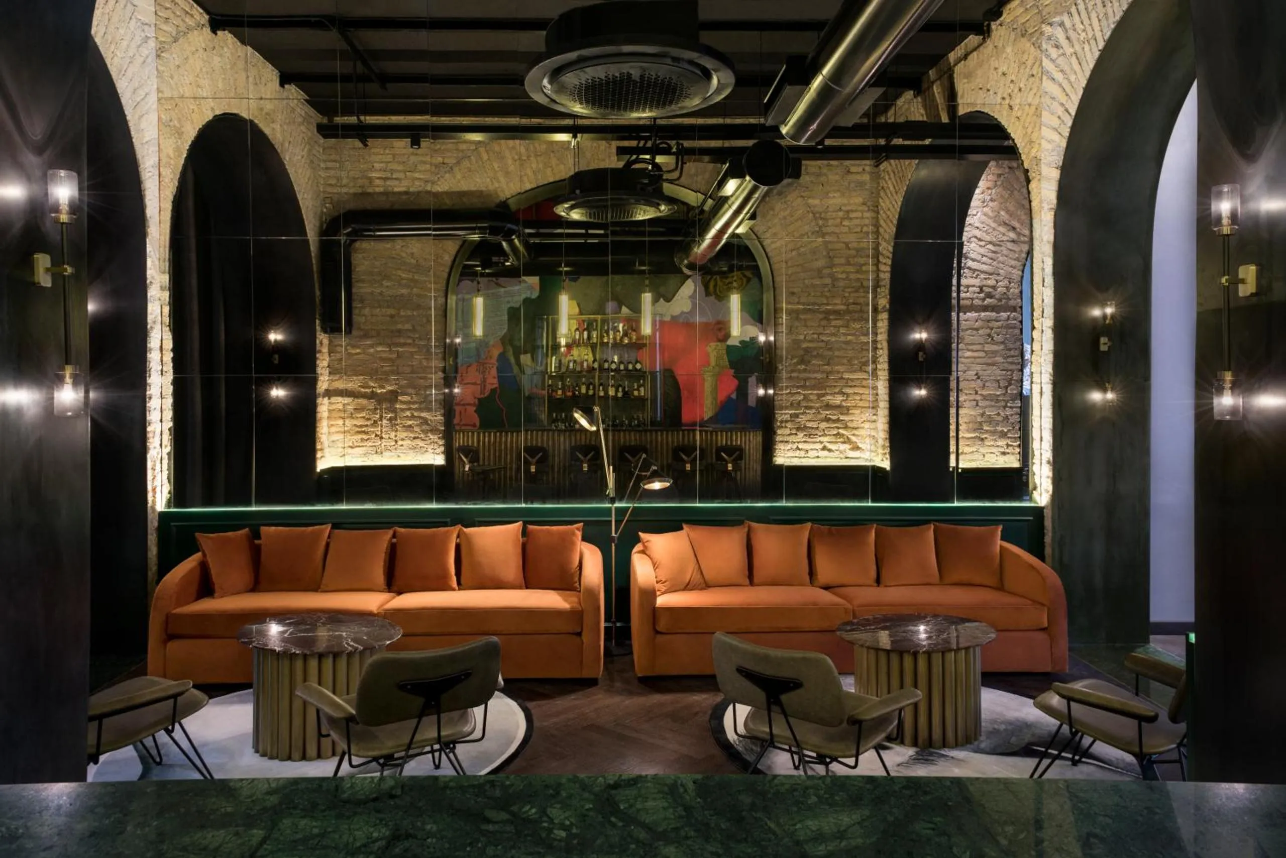 Chapter Roma lounge with orange velvet sofas, exposed brick vaulted arches and brass detailing