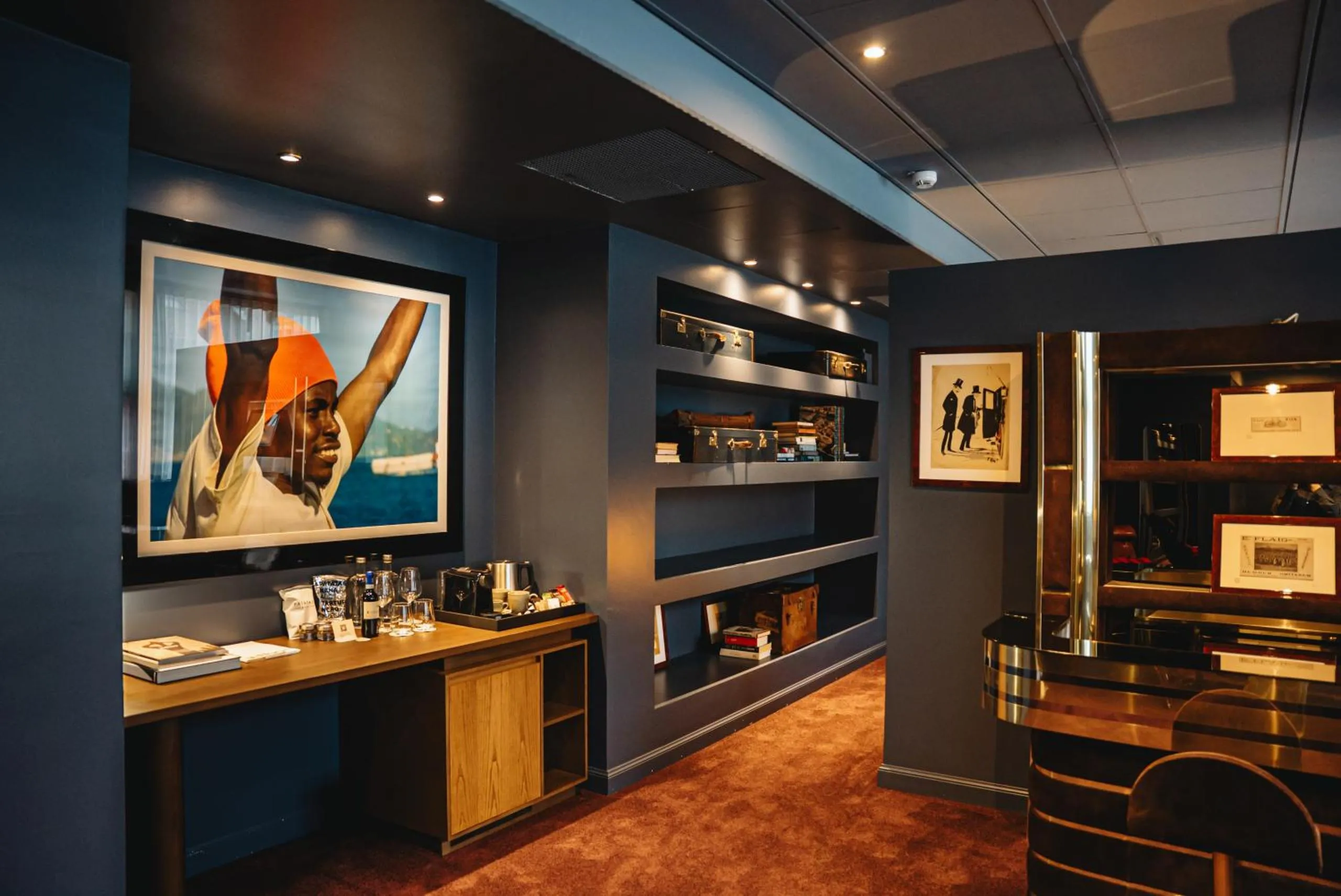 Aethos Milan lounge with deep blue walls, vintage trunks, framed swimmer portrait and polished brass bar