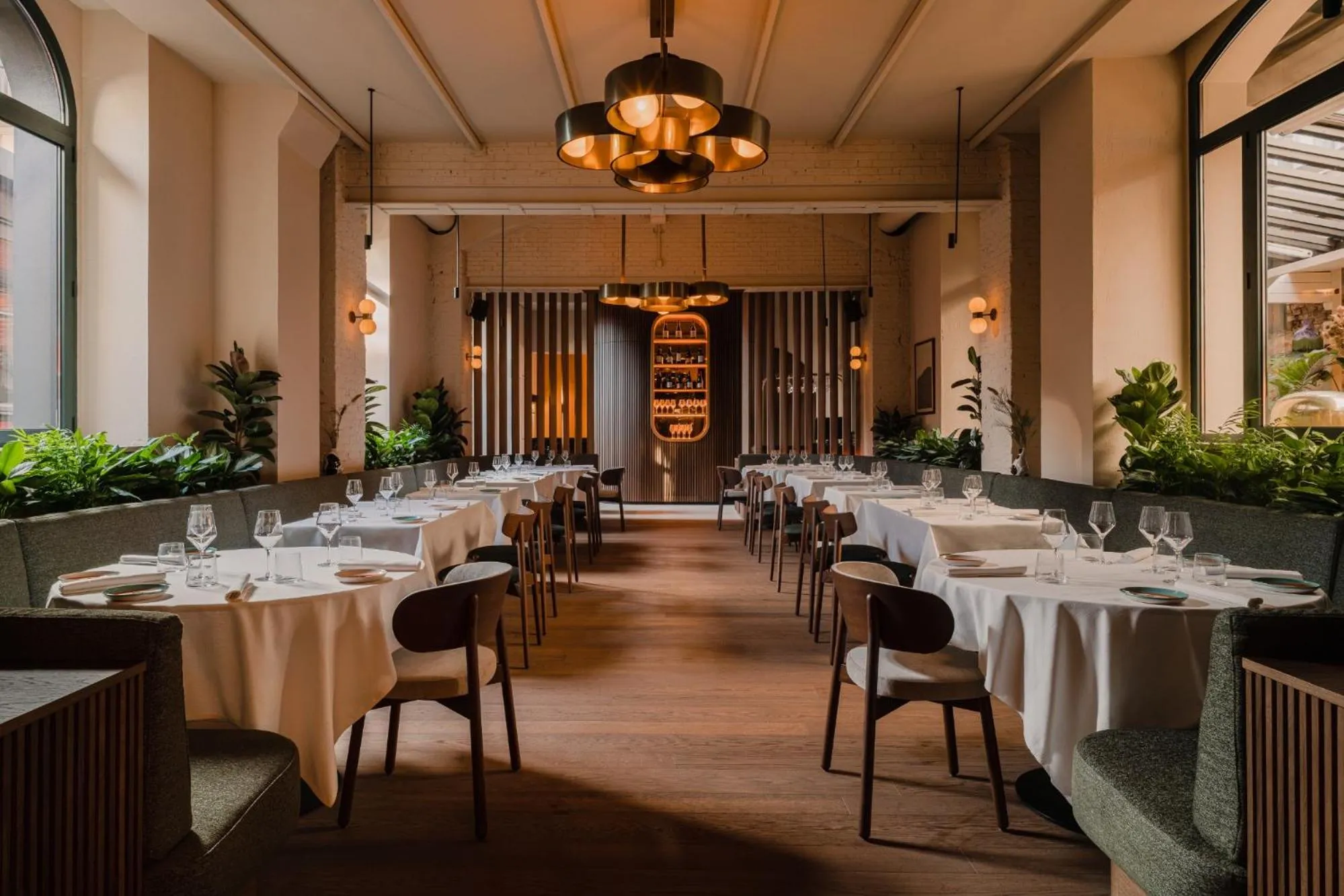 Aethos Milan restaurant with brass globe chandeliers, green banquettes, white tablecloths and arched windows