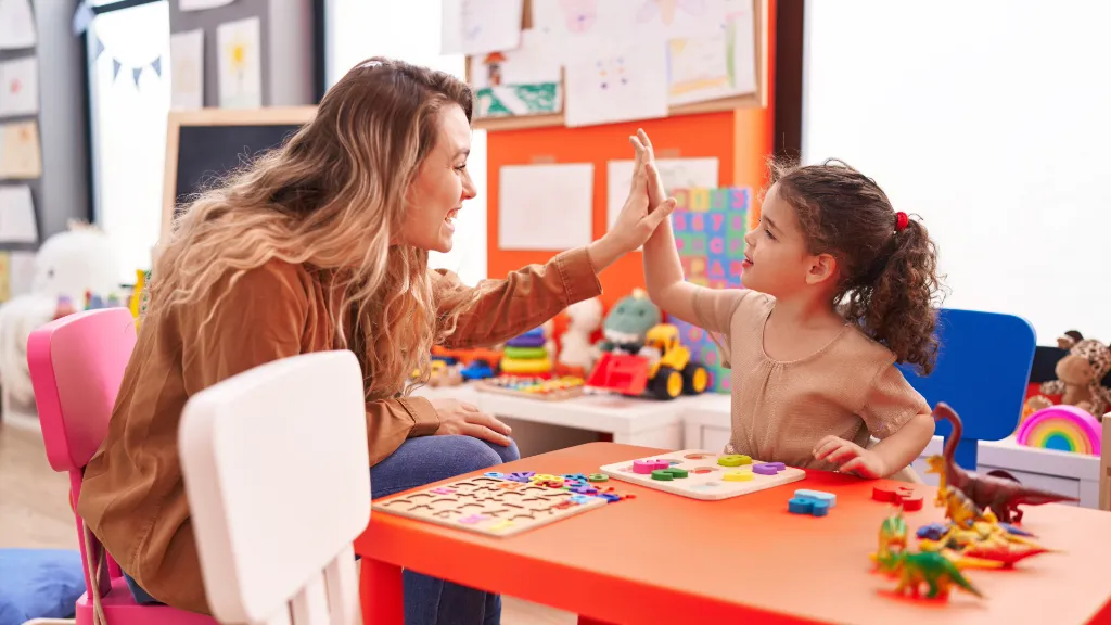 Młoda nauczycielka w przedsazkolu radośnie przybija pitkę z dziewczynką.