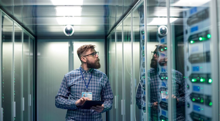 IT technician inspecting servers in a data center while holding a tablet.
