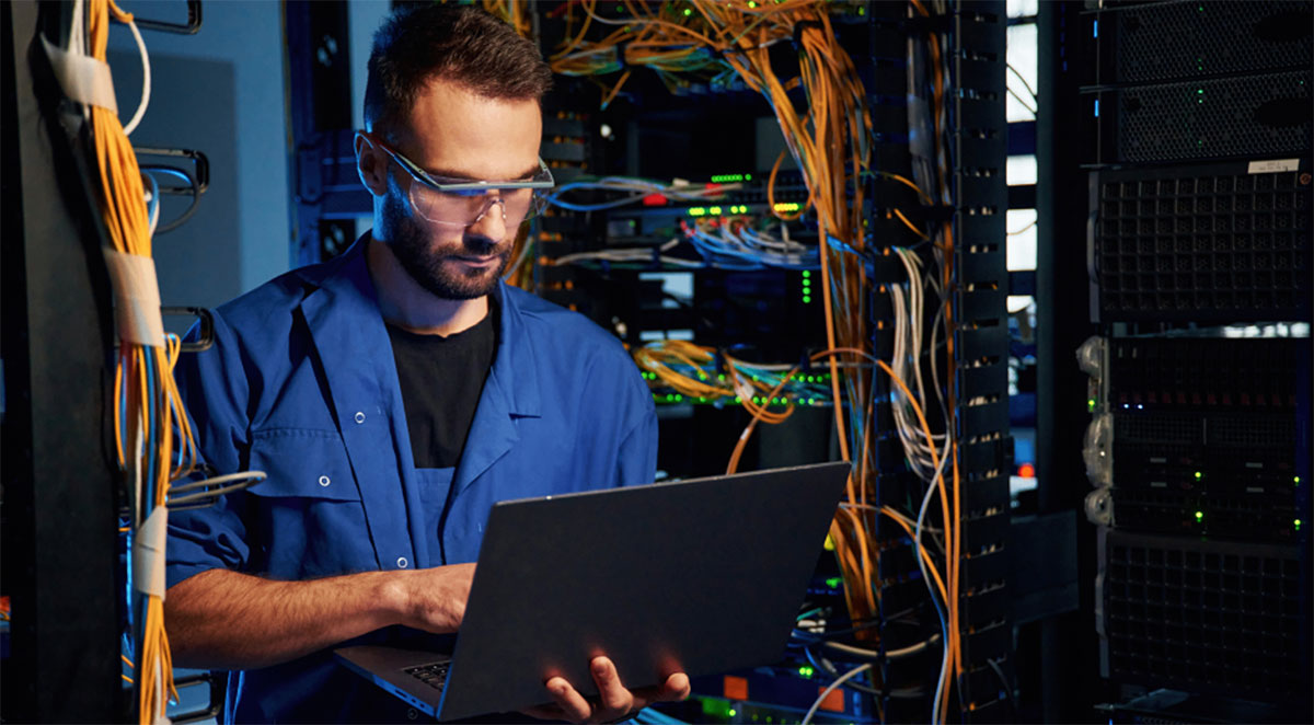 IT technician working on a laptop in a server room.
