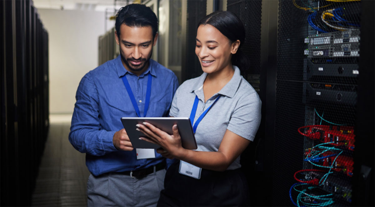IT technicians reviewing network infrastructure data on a tablet in a server room