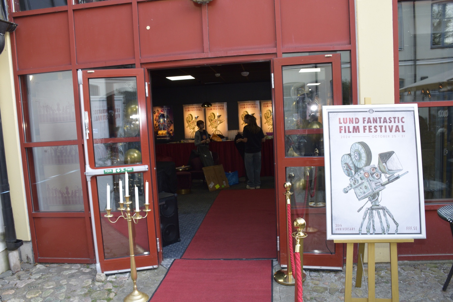 Entrance to a film festival venue with a red carpet, a five-armed gold candelabra, and a poster for the Lund Fantastic Film Festival 2024.