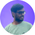 Man with beard and glasses smiling, wearing a light green T-shirt, with a purple gradient background.
