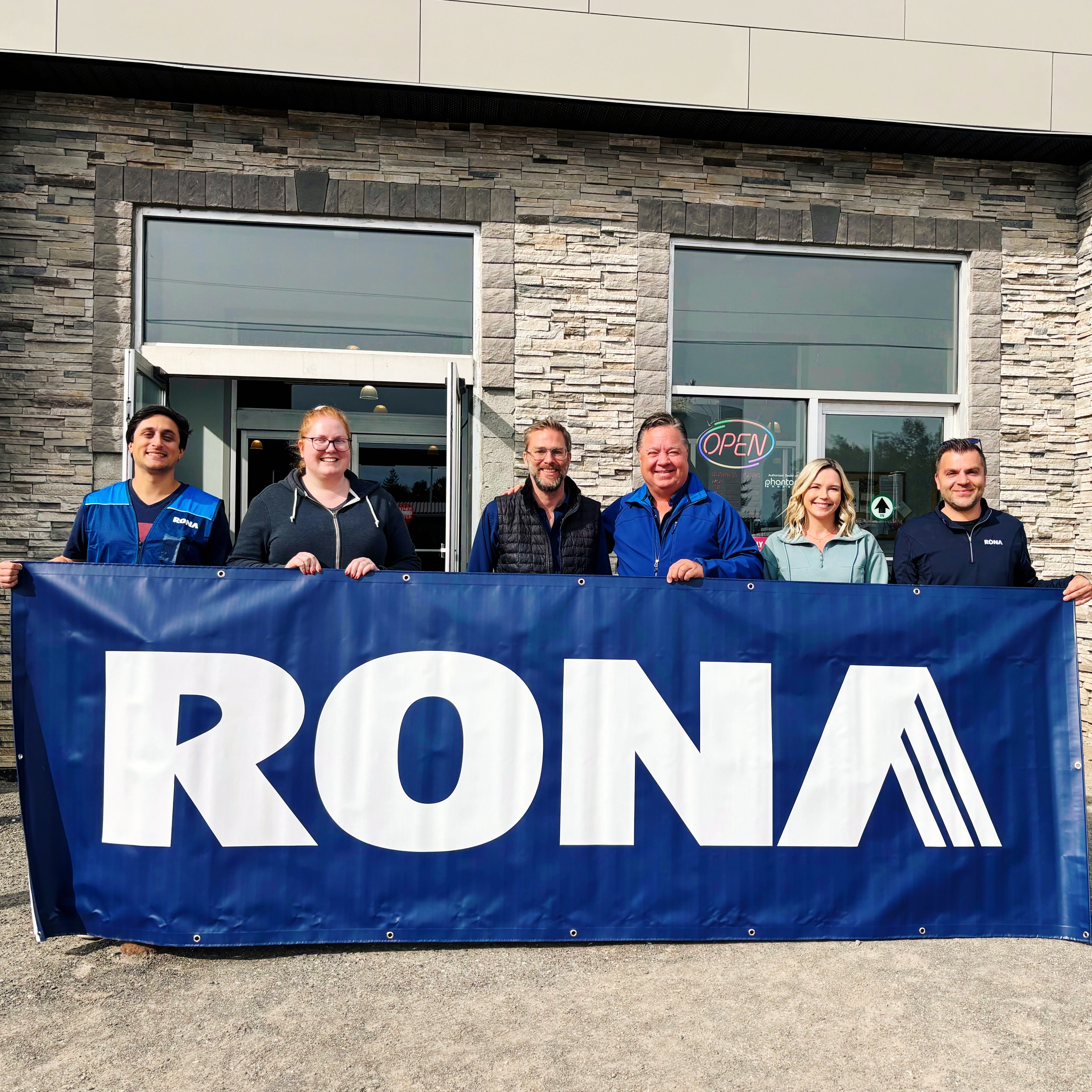 People standing in front of brick store holding RONA banner